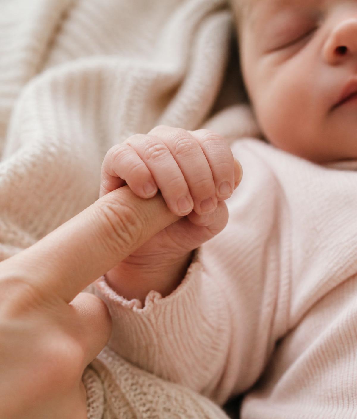 A newborn's tiny hand curled around a parent's finger